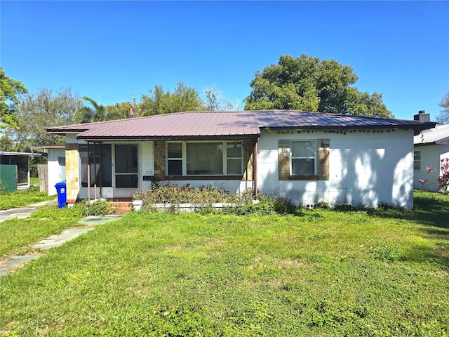 view of front of property with metal roof, concrete block siding, a front lawn, and a sunroom