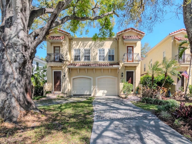 mediterranean / spanish-style house featuring stucco siding, driveway, a tile roof, a garage, and a balcony