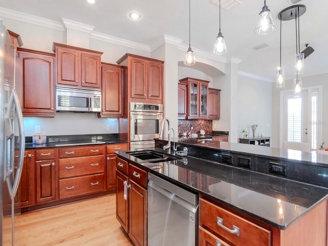 kitchen with light wood finished floors, a kitchen island with sink, decorative light fixtures, stainless steel appliances, and a sink