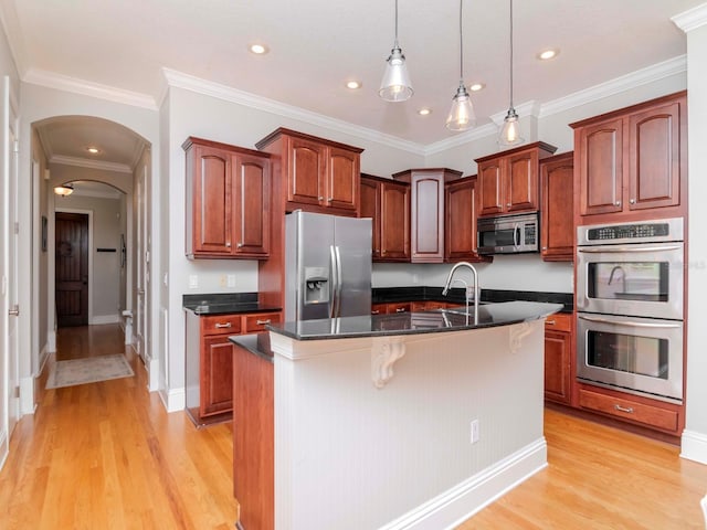 kitchen featuring a center island with sink, light wood finished floors, arched walkways, a sink, and appliances with stainless steel finishes