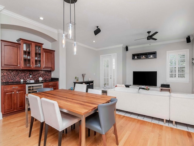 dining area with light wood-type flooring, wine cooler, ceiling fan, and crown molding