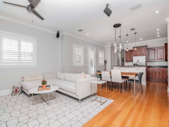 living area featuring visible vents, plenty of natural light, a ceiling fan, and crown molding