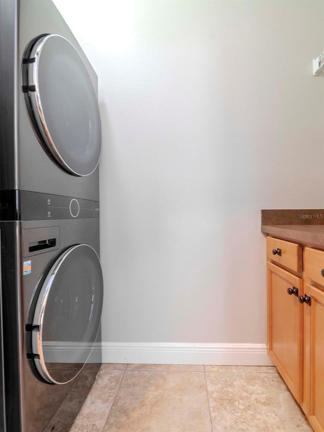 washroom with light tile patterned floors, cabinet space, stacked washer / drying machine, and baseboards