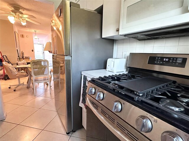 kitchen with light tile patterned floors, light countertops, backsplash, white microwave, and gas stove