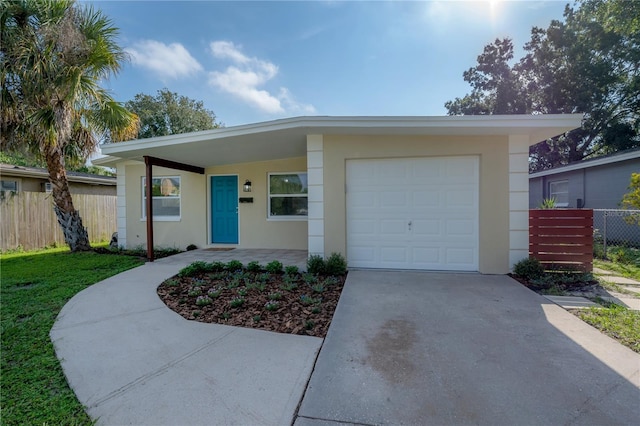 mid-century modern home with a garage, concrete driveway, fence, and stucco siding