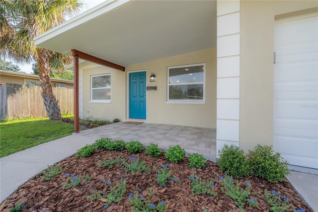 property entrance with a yard, fence, and stucco siding