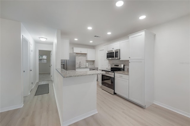 kitchen featuring light wood finished floors, stainless steel appliances, backsplash, a sink, and light stone countertops