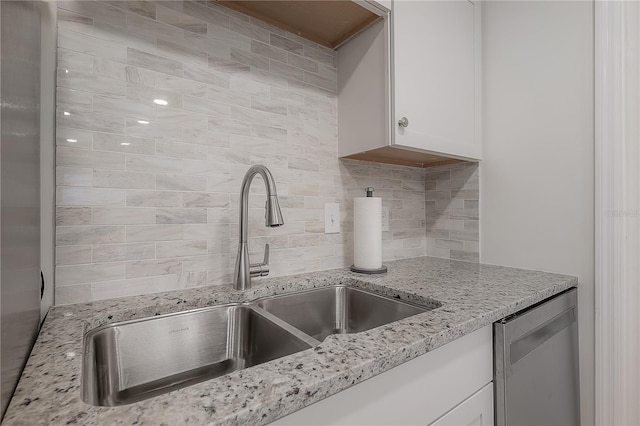 kitchen featuring light stone counters, backsplash, white cabinetry, a sink, and dishwasher