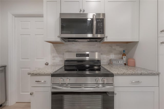 kitchen featuring light stone countertops, white cabinetry, stainless steel appliances, and backsplash