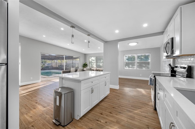 kitchen with a healthy amount of sunlight, light wood-style floors, appliances with stainless steel finishes, and lofted ceiling