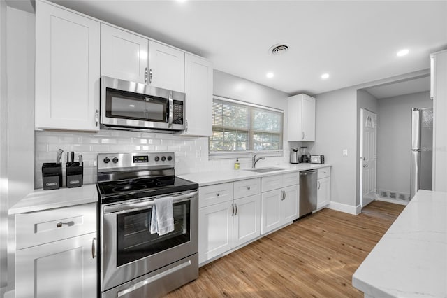 kitchen featuring light wood finished floors, visible vents, decorative backsplash, appliances with stainless steel finishes, and a sink