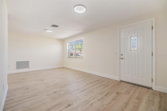 foyer entrance with visible vents, baseboards, light wood-style floors, and a textured ceiling