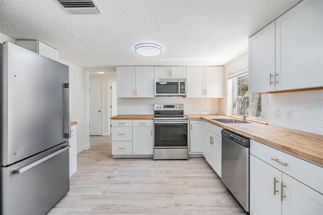 kitchen featuring visible vents, a sink, stainless steel appliances, wood counters, and light wood-type flooring