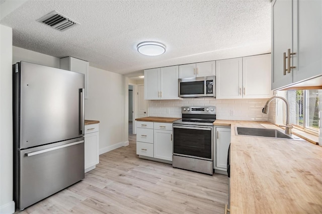 kitchen featuring visible vents, wooden counters, light wood-type flooring, stainless steel appliances, and a sink