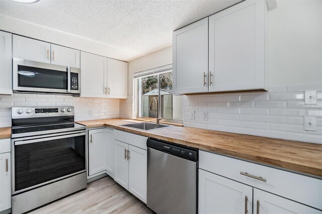 kitchen with a sink, white cabinets, appliances with stainless steel finishes, tasteful backsplash, and butcher block counters