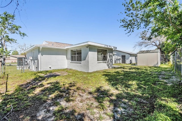 back of house with fence, a shed, a yard, stucco siding, and an outdoor structure