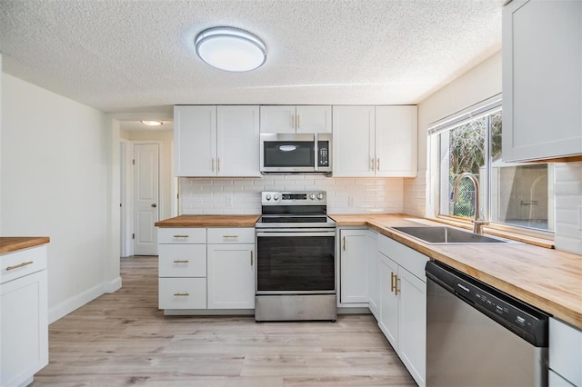 kitchen featuring light wood-style flooring, a sink, decorative backsplash, appliances with stainless steel finishes, and butcher block counters