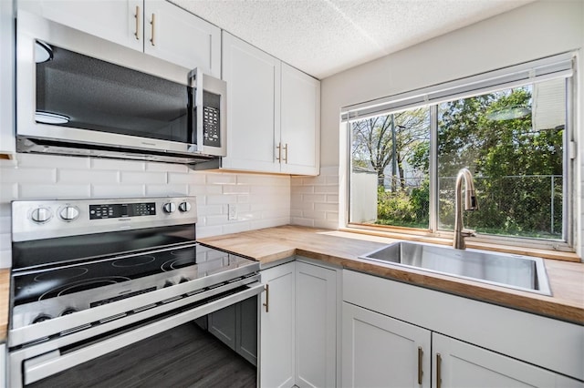 kitchen featuring a sink, stainless steel appliances, a textured ceiling, wood counters, and tasteful backsplash