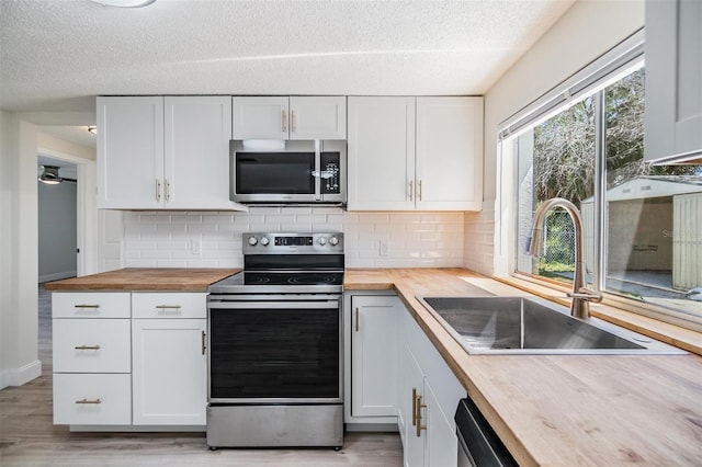 kitchen with light wood finished floors, wooden counters, a sink, appliances with stainless steel finishes, and white cabinetry