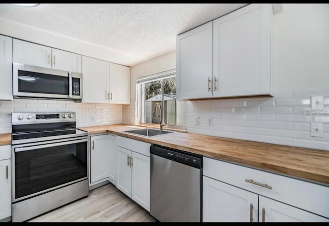 kitchen with a sink, decorative backsplash, butcher block countertops, stainless steel appliances, and white cabinetry