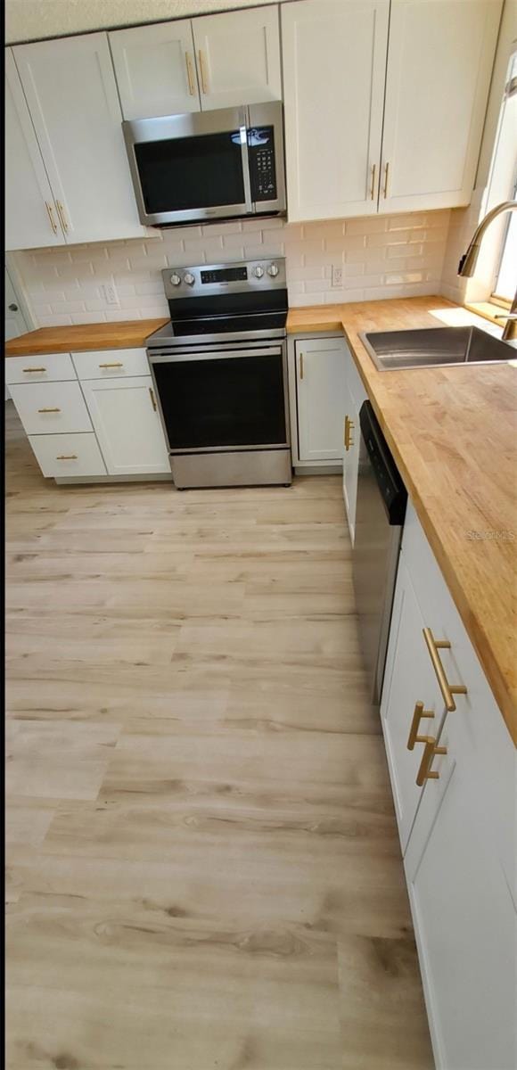 kitchen featuring a sink, wood counters, backsplash, appliances with stainless steel finishes, and light wood finished floors