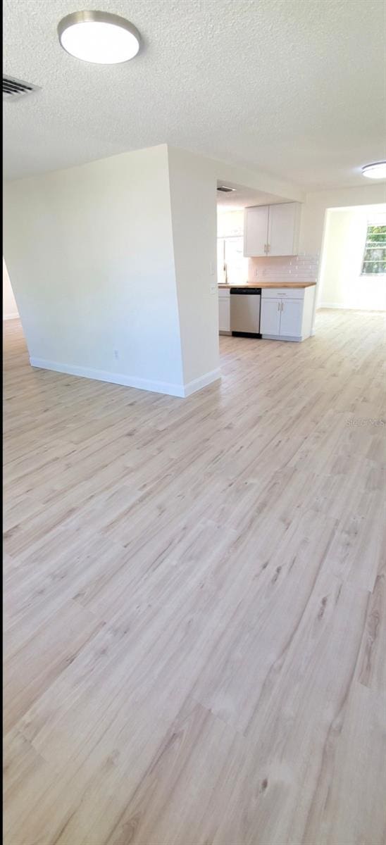 unfurnished living room with visible vents, baseboards, a textured ceiling, and light wood finished floors