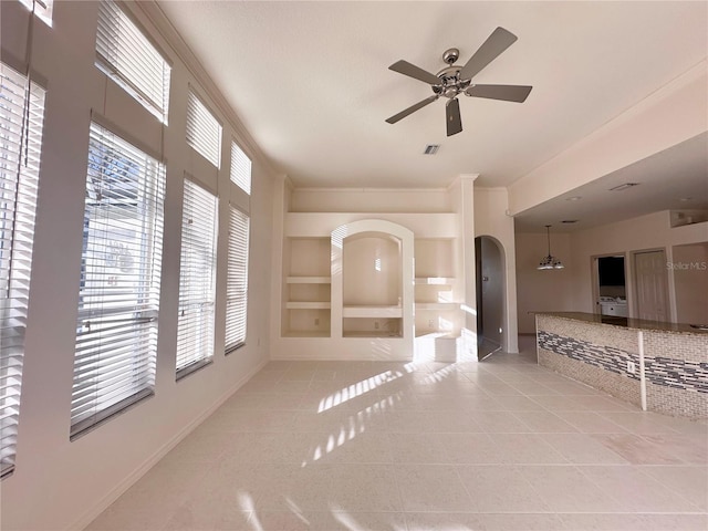 tiled spare room with built in shelves, arched walkways, crown molding, visible vents, and a ceiling fan