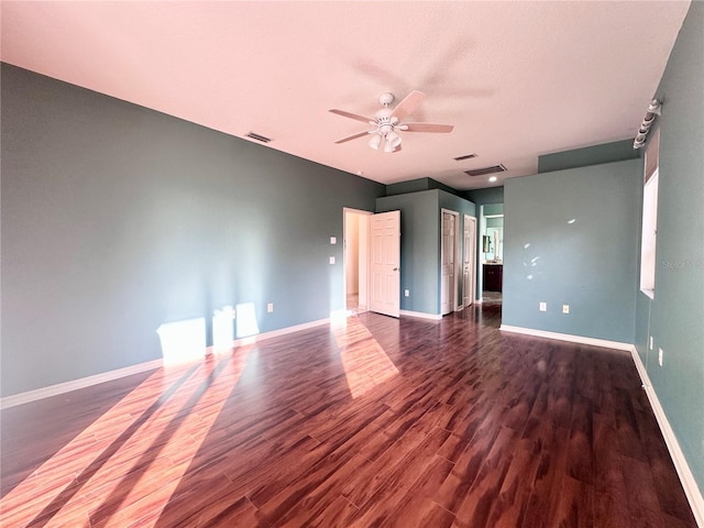 empty room featuring dark wood-type flooring, visible vents, ceiling fan, and baseboards