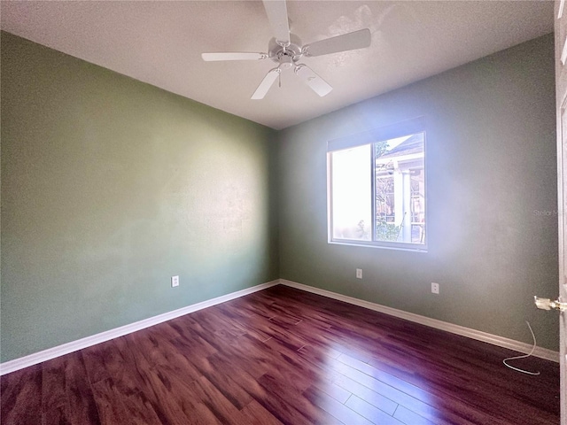 empty room with dark wood finished floors, a ceiling fan, and baseboards