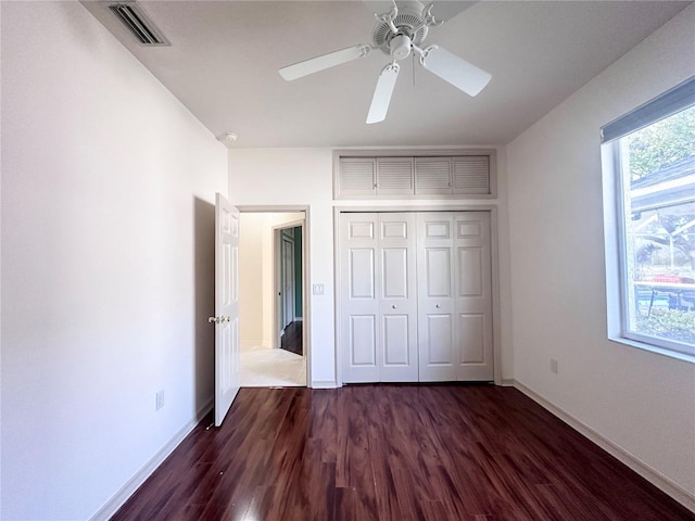 unfurnished bedroom featuring dark wood-type flooring, multiple windows, a closet, and visible vents