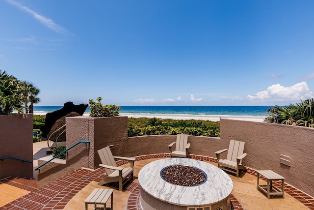 view of patio / terrace featuring a water view, a beach view, and a fire pit