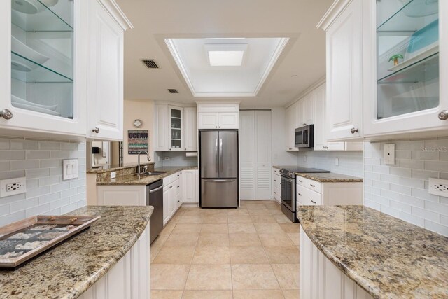 kitchen featuring visible vents, light stone counters, stainless steel appliances, white cabinetry, and a sink