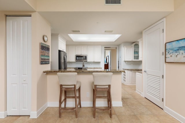 kitchen featuring white cabinets, decorative backsplash, a kitchen breakfast bar, a peninsula, and stainless steel appliances