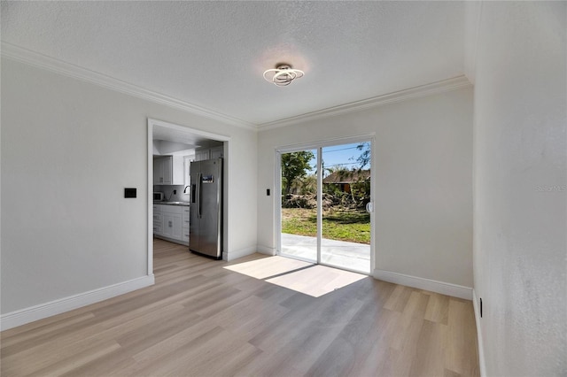 empty room featuring baseboards, crown molding, a textured ceiling, and light wood finished floors