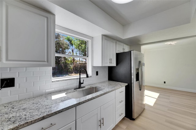 kitchen with a sink, baseboards, light wood-style floors, backsplash, and stainless steel fridge with ice dispenser