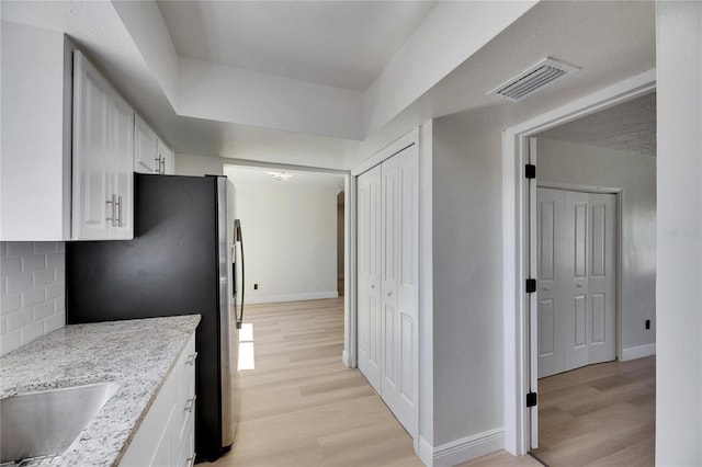 kitchen with light wood-type flooring, white cabinetry, visible vents, and decorative backsplash