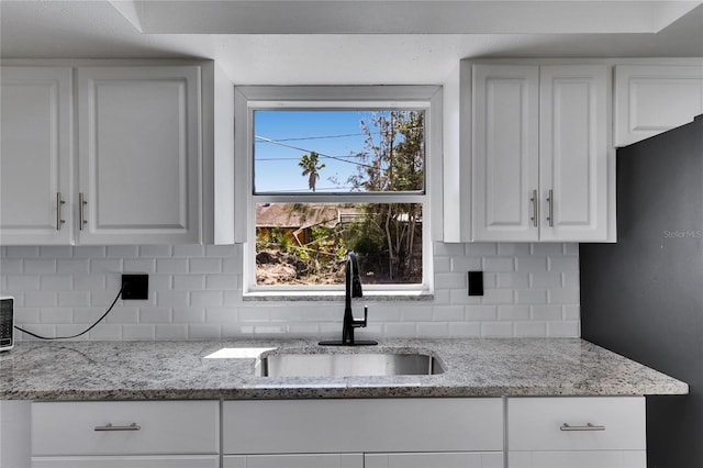 kitchen with freestanding refrigerator, white cabinetry, a sink, and decorative backsplash