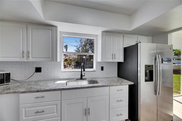 kitchen featuring white cabinets, light stone counters, appliances with stainless steel finishes, a sink, and backsplash