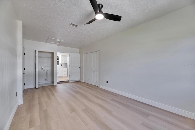 unfurnished bedroom with visible vents, light wood-style flooring, attic access, a textured ceiling, and baseboards