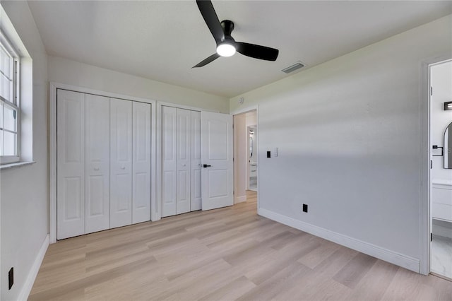 unfurnished bedroom featuring ensuite bathroom, light wood-style flooring, visible vents, baseboards, and multiple closets