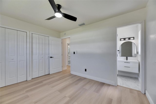 unfurnished bedroom with ensuite bathroom, light wood-style flooring, visible vents, baseboards, and two closets