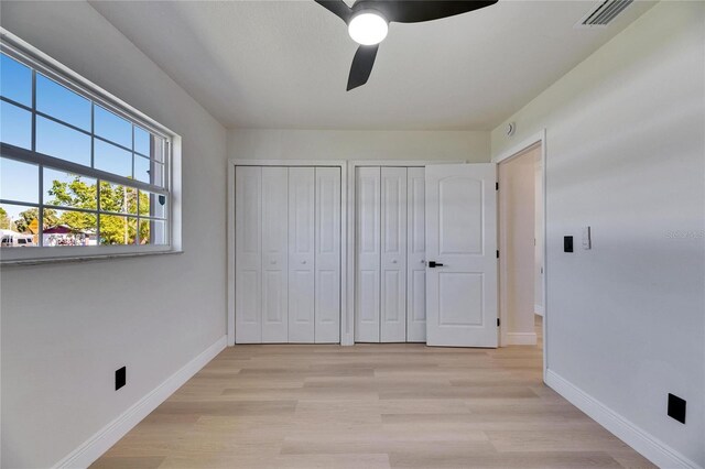 unfurnished bedroom featuring light wood-style floors, visible vents, baseboards, and two closets