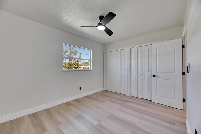 unfurnished bedroom featuring baseboards, light wood-style flooring, ceiling fan, a textured ceiling, and two closets