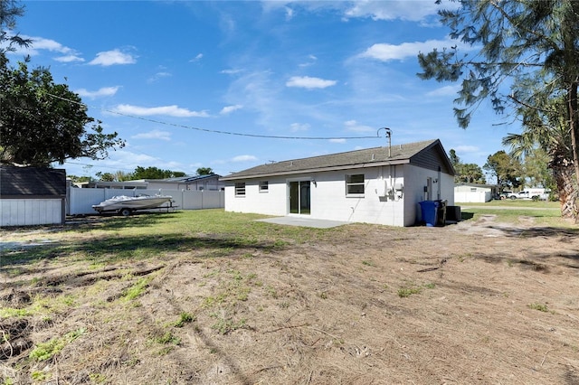 rear view of property with a patio, concrete block siding, an outbuilding, fence, and a yard