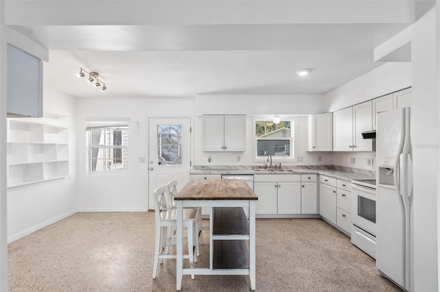 kitchen featuring white cabinetry, baseboards, white appliances, light speckled floor, and a sink