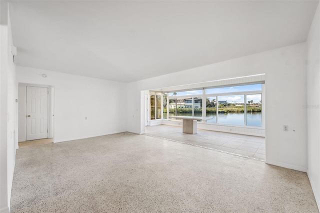 spare room with speckled floor, a water view, and baseboards