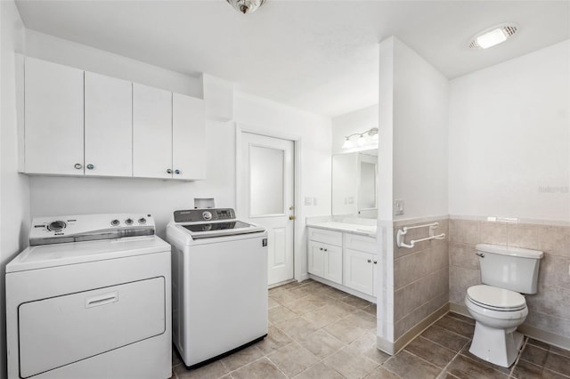 washroom with washer and clothes dryer, tile walls, light tile patterned flooring, wainscoting, and laundry area