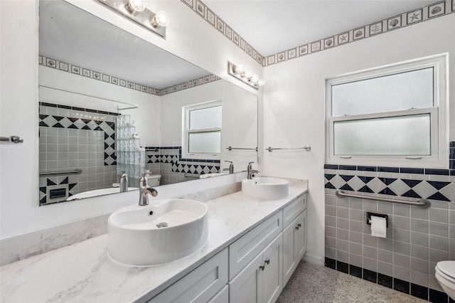 bathroom featuring tile walls, toilet, speckled floor, and a sink