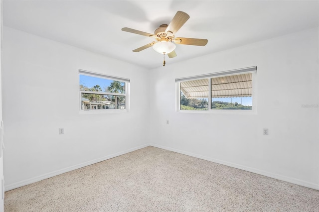 unfurnished room featuring speckled floor, baseboards, and ceiling fan