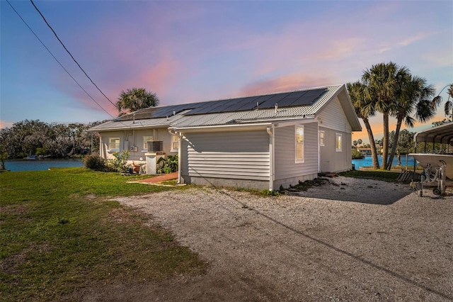 front of property at dusk featuring a yard, a water view, gravel driveway, and metal roof